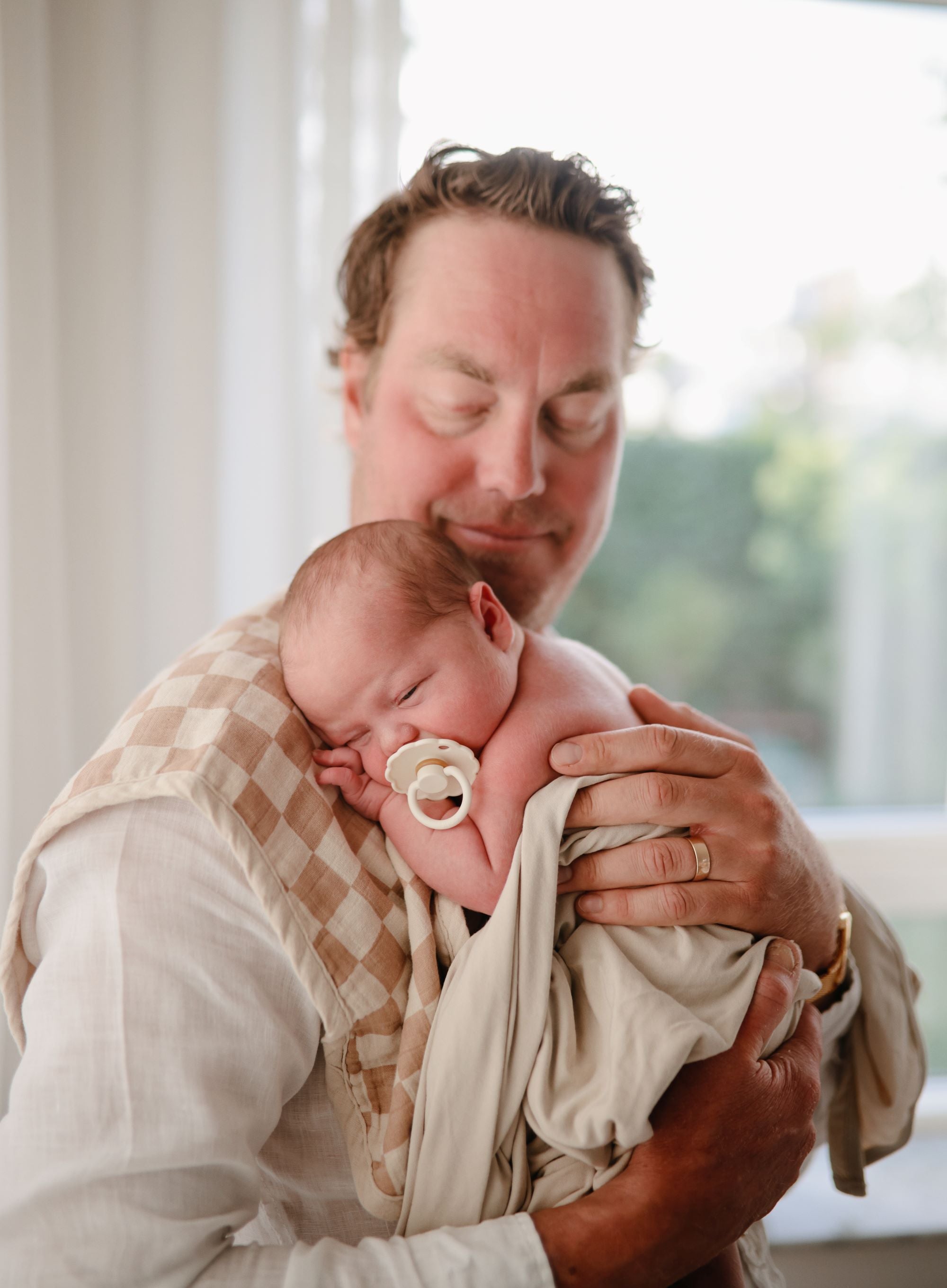 A father burping a newborn baby in Mushie Burb Cloth and Frigg pacifier. Blog by Mummasphere.com.